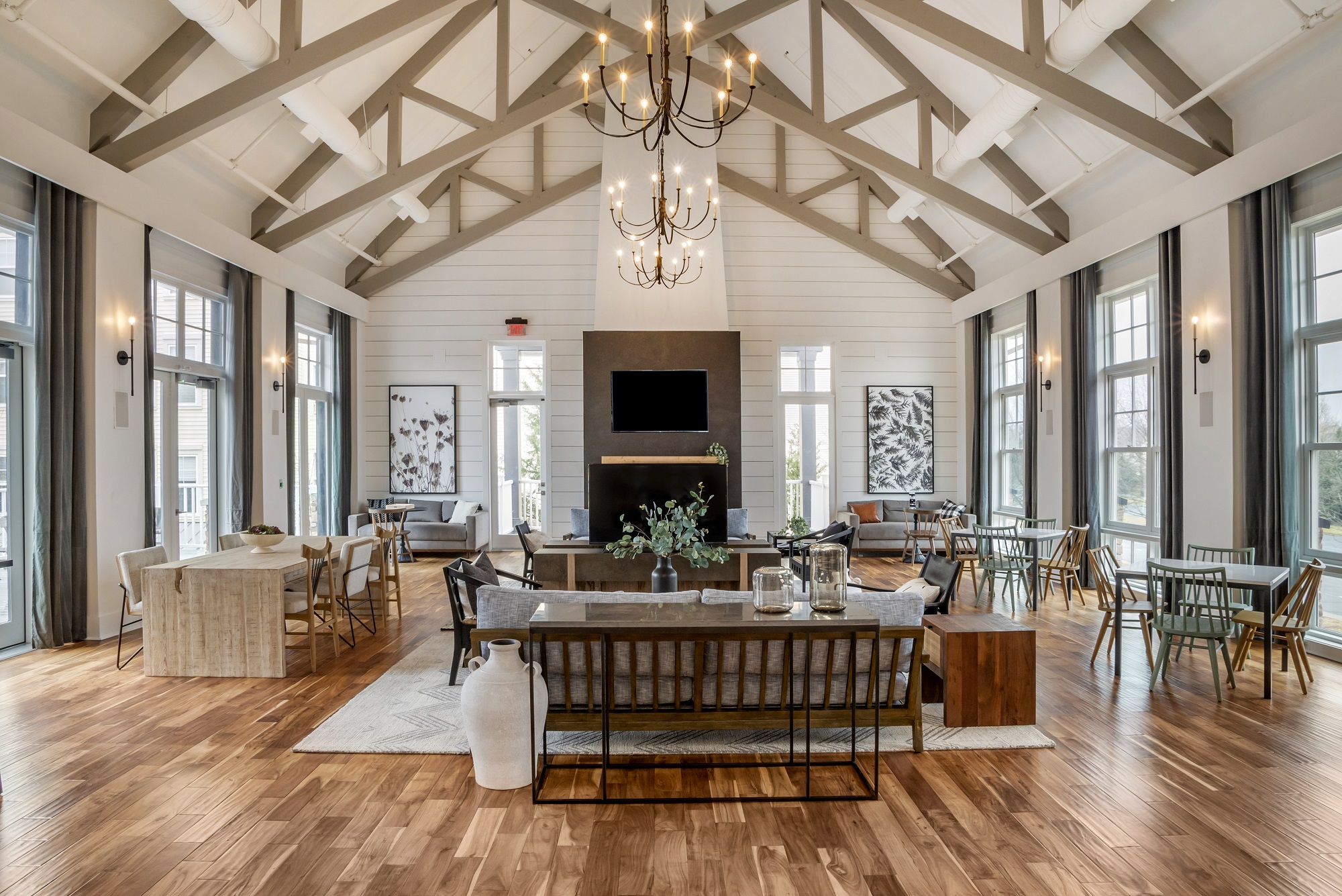 Indoor clubhouse lounge area with couches, table seating, TVs, designer lighting, and wood-style flooring