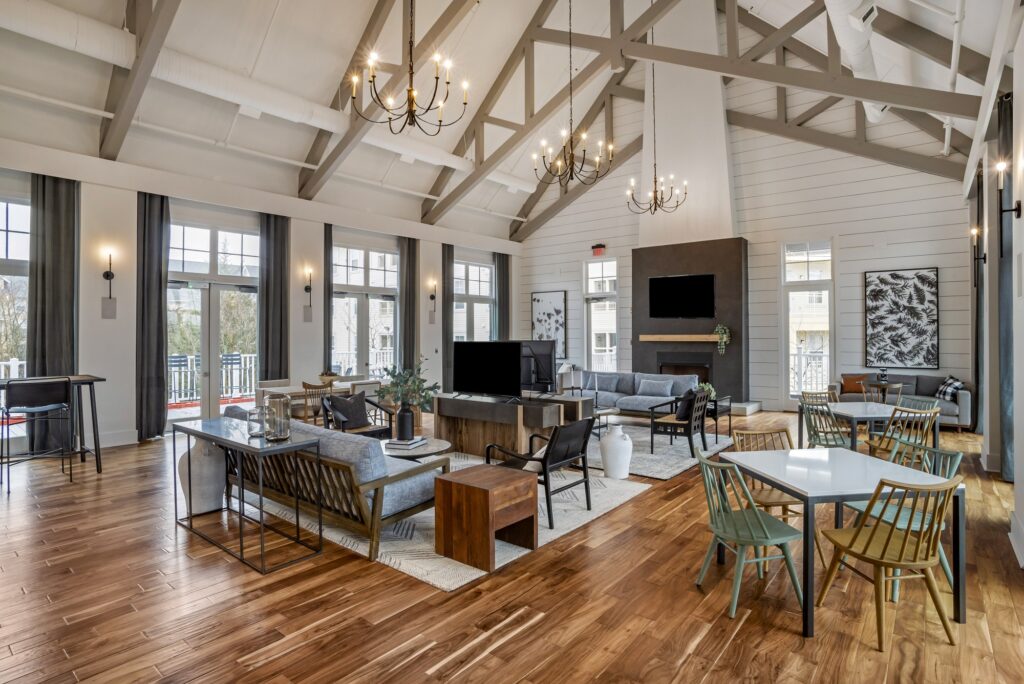 Indoor clubhouse lounge area with couches, table seating, TVs, fire pit, designer lighting, and wood-style flooring