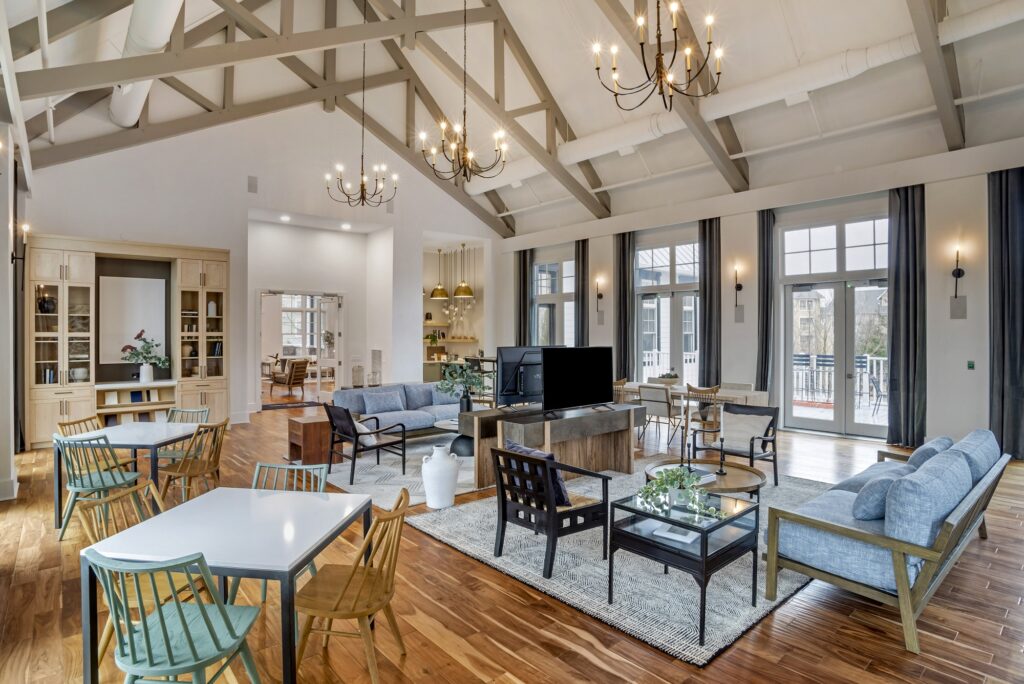 Indoor clubhouse lounge area with couches, table seating, TVs, designer lighting, and wood-style flooring