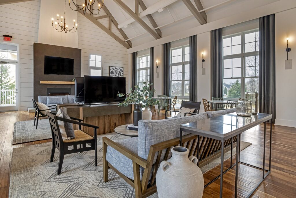 Indoor clubhouse lounge area with couches, table seating, TVs, fire pit, designer lighting, and wood-style flooring