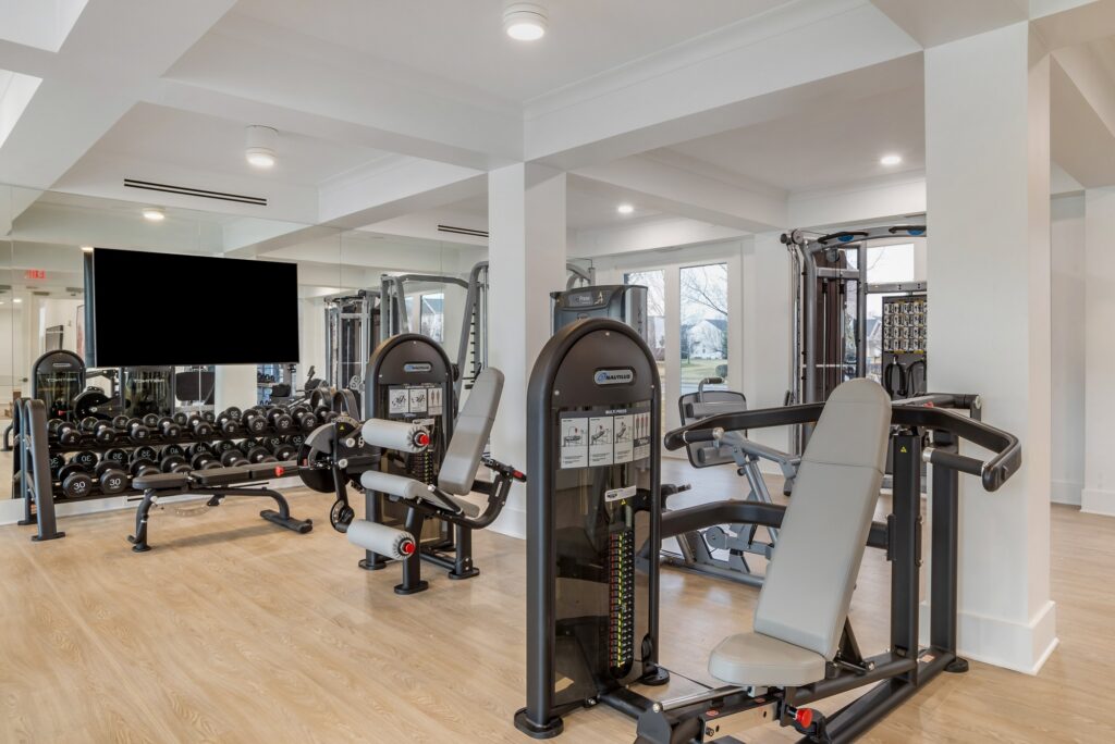 Indoor gym area with weight machines, outdoor lighting, TV, and wood-style flooring