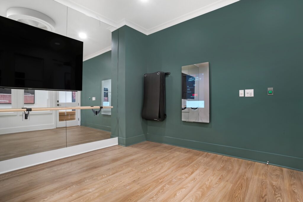 Indoor workout studio with large mirror, TV, wood-style flooring, and accent colored walls