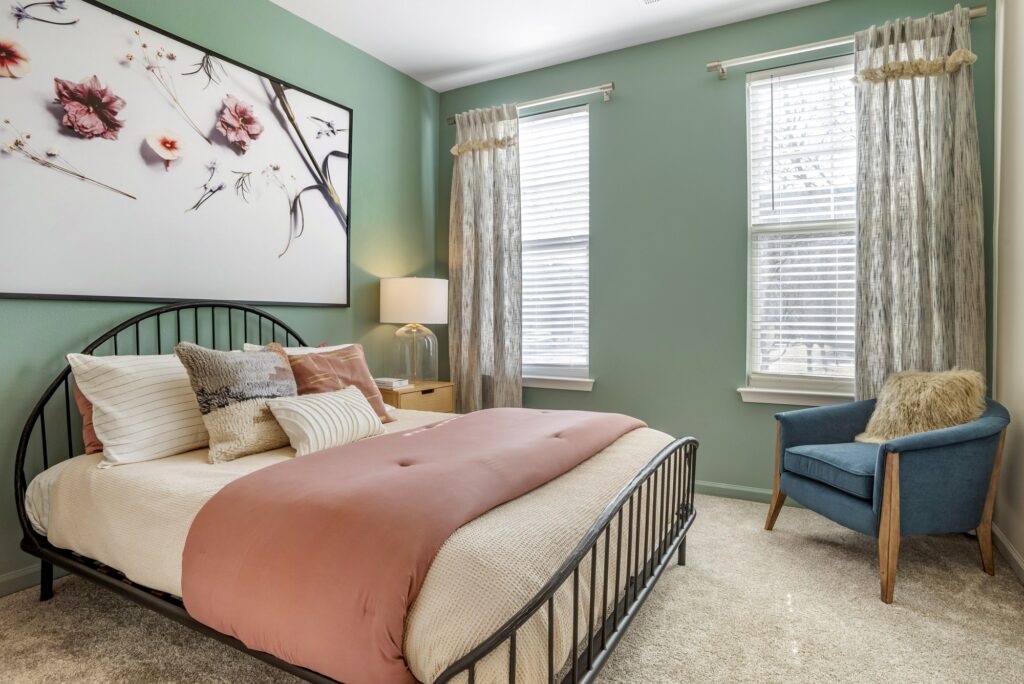 Bedroom with queen size bed, accent colored walls, lamps, windows, and carpet flooring