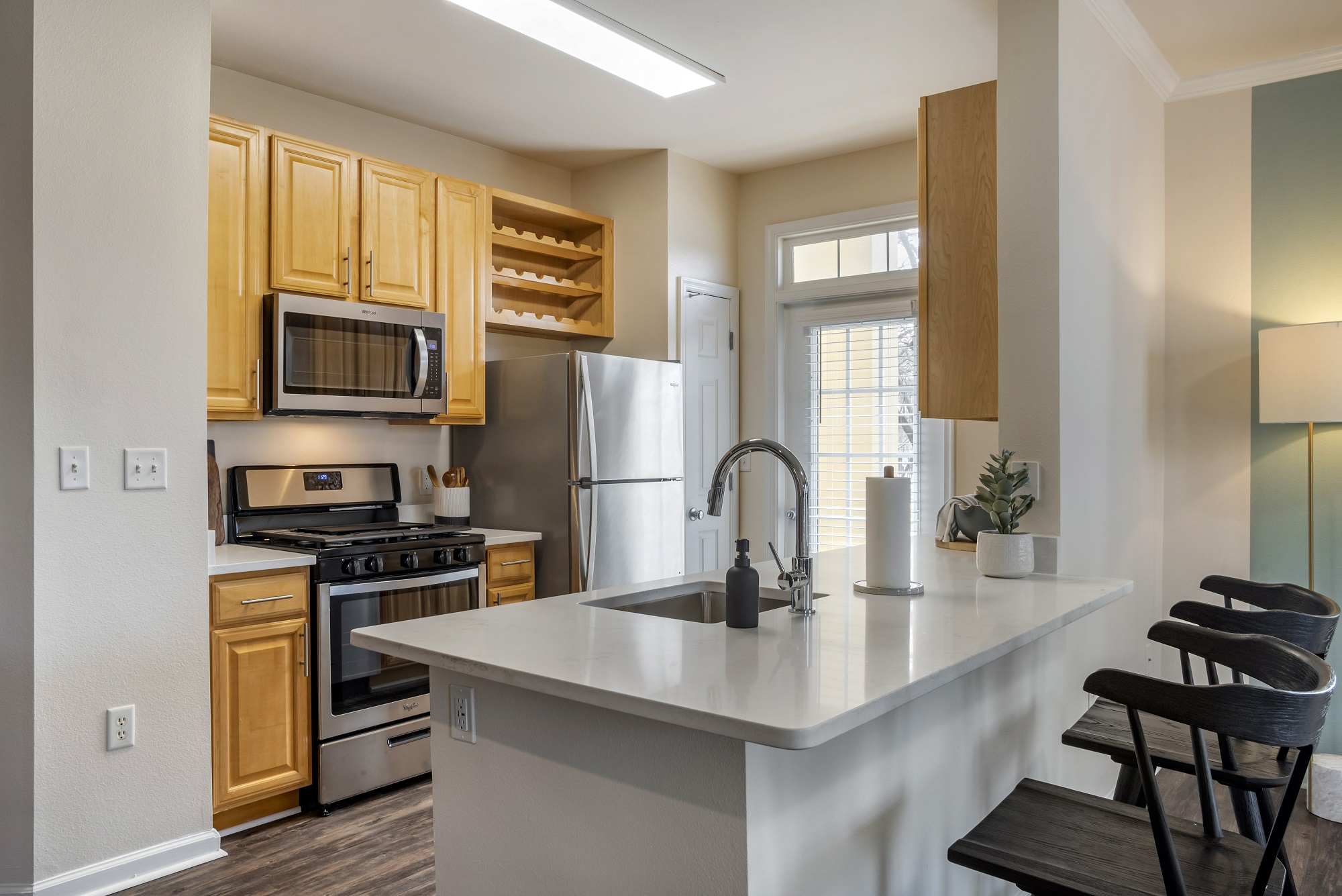 Kitchen area with island sink, stainless steel appliances, patio access, designer lighting, and wood-style flooring