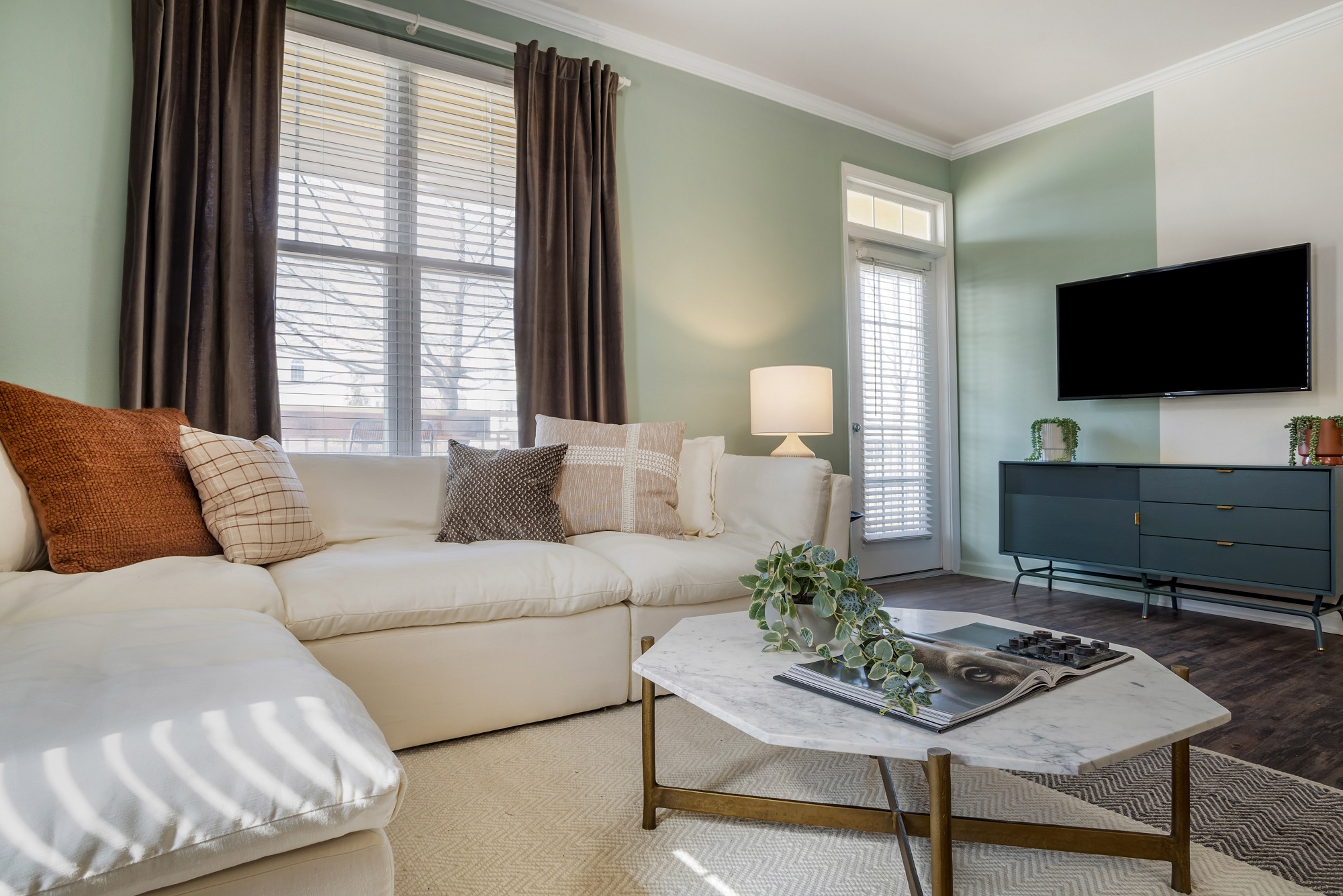 Living room with couch, window lighting, TV, accent colored walls, and wood-style flooring